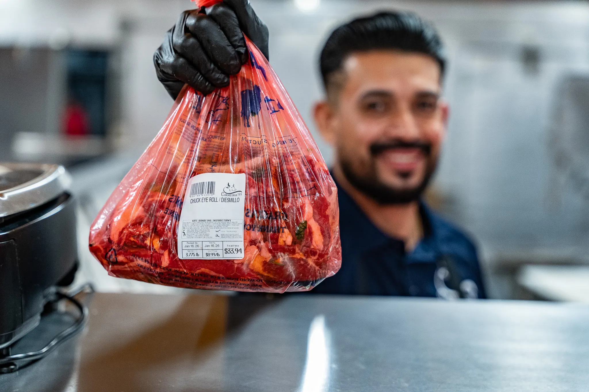 Smiling Carnicería 99 butcher holding up a bag of fresh marinated meat