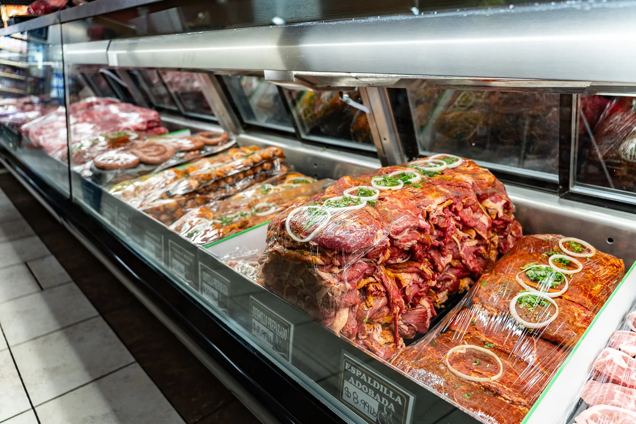 Full butcher case of fresh and marinated meats at the Carnicería 99 counter