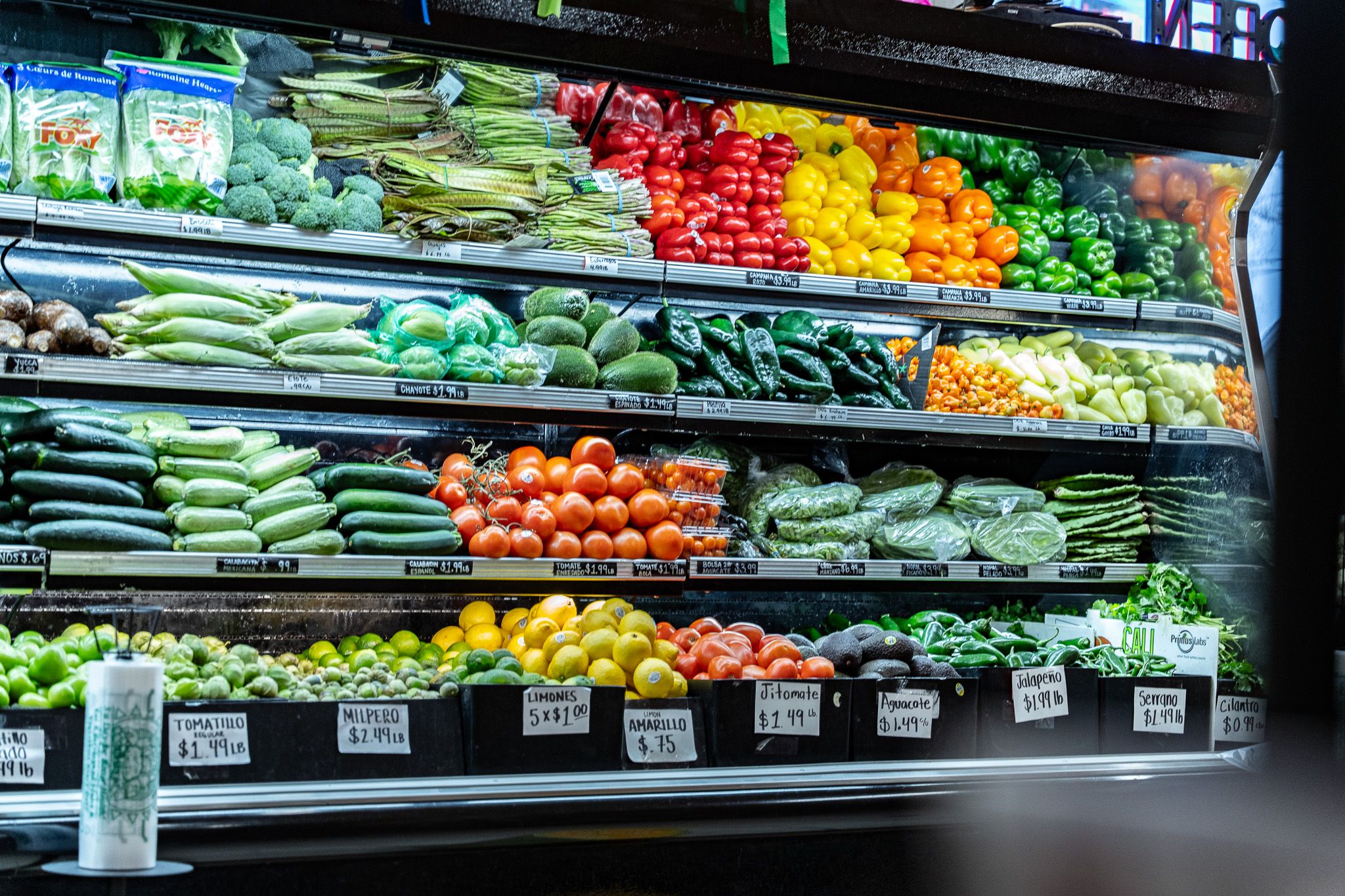 Open refrigerated produce case stocked with fresh vegetables and fruit at Carnicería 99