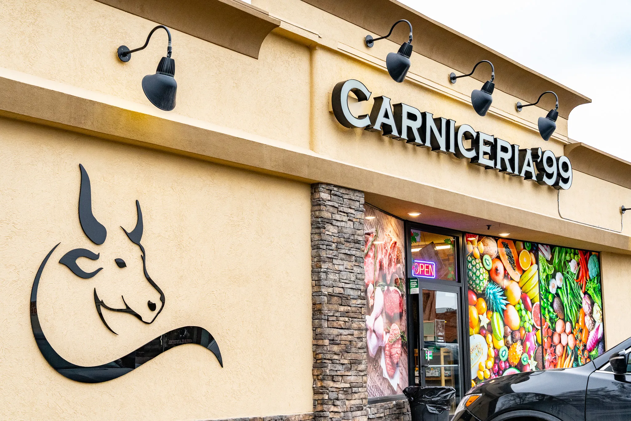 Exterior corner of Carnicería 99 in Hermiston showing the lit storefront sign and the black bull-head logo on the wall